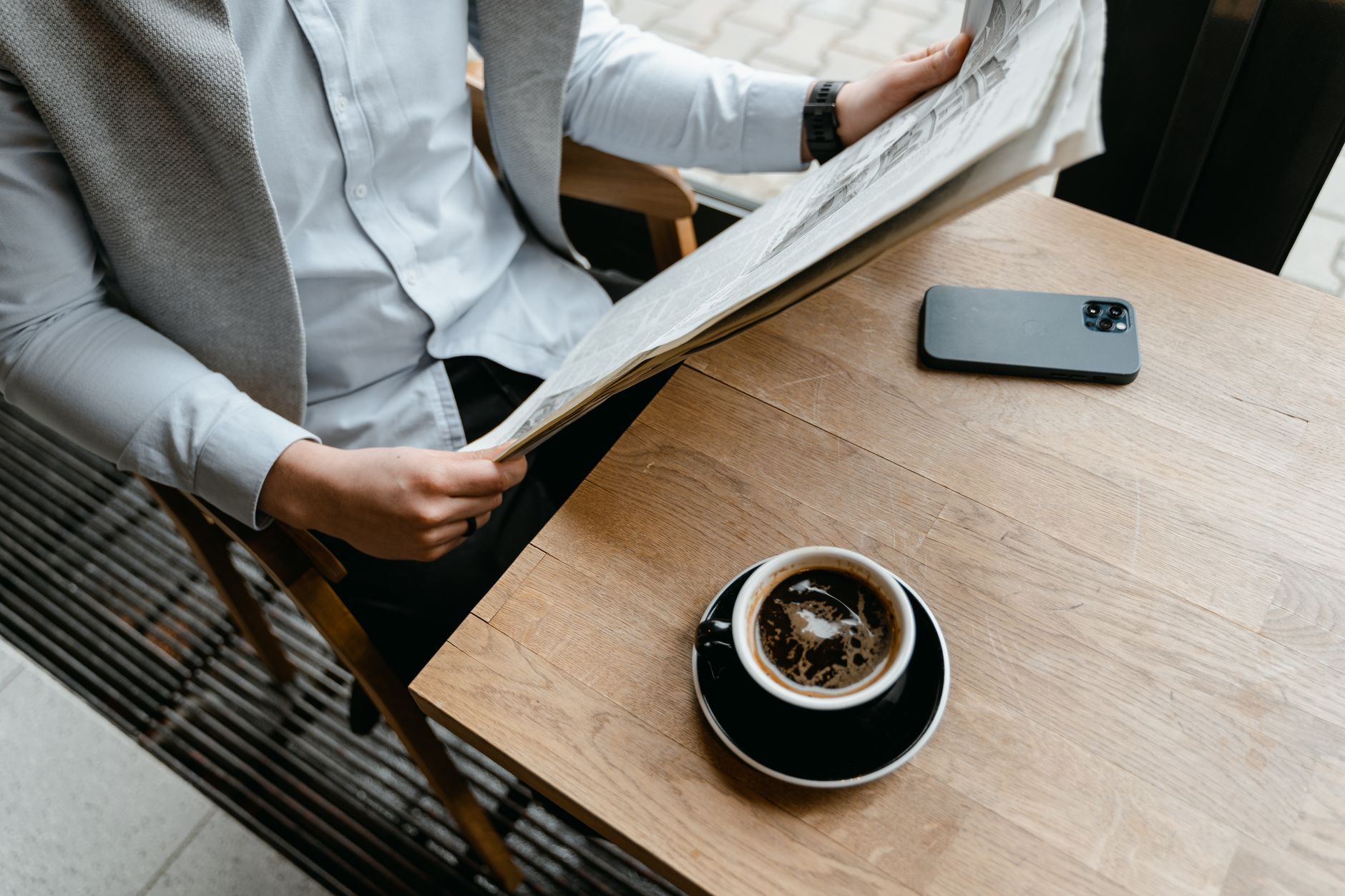 An adult male enjoying his coffee while reading a newspaper at a cafe with his smartphone nearby. — Erfahrungsbericht: Ares C